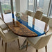 A stunning oval resin river table surrounded by cream chairs with a city view background.