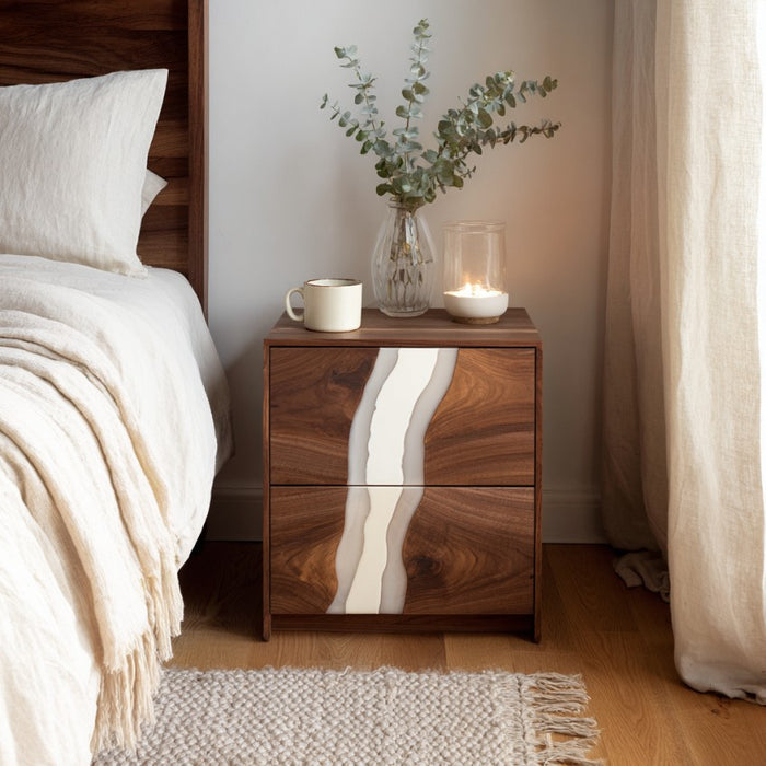 Wooden nightstand with decorative items next to a bed in a bedroom.