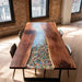 Wooden dining table with a colorful glass inset in a room with brick walls and large windows.