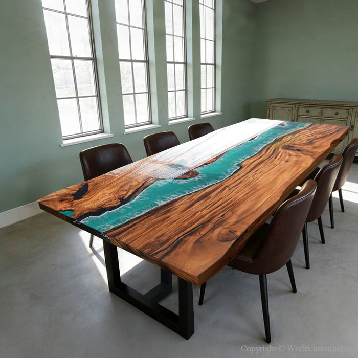 Wooden dining table with a river design, surrounded by chairs in a room with large windows.