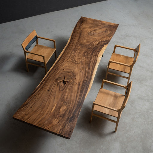 Top view of a natural walnut live edge wood slab dining table with rich wood grain texture, surrounded by four minimalist wooden chairs on a concrete floor.