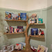 Wooden tree-shaped bookshelf with children's books and toys against a light green wall.