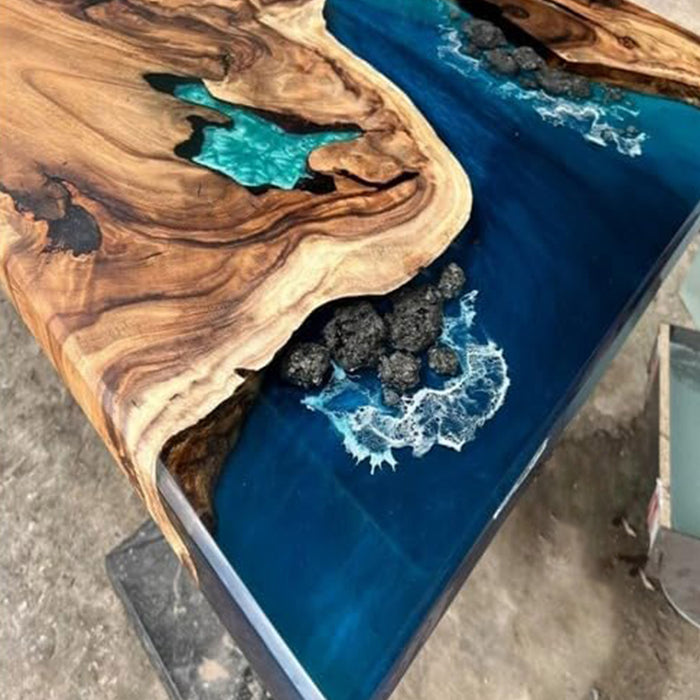 Wooden table with blue resin and decorative elements on a concrete floor.