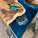 Wooden table with blue resin and decorative elements on a concrete floor.