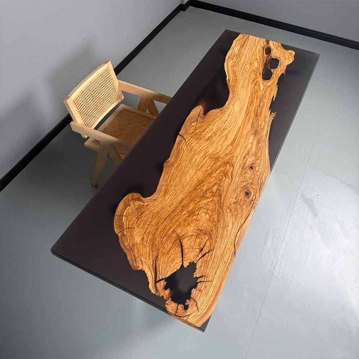 Wooden desk with natural grain and black resin inclusions, accompanied by a wicker chair on a gray floor.