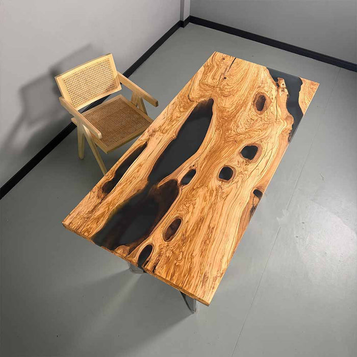 Wooden table with natural grain and black resin inclusions next to a wicker chair on a gray floor.