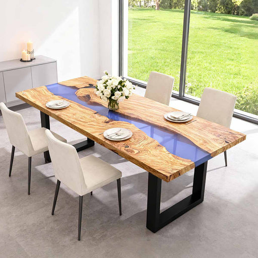 Dining table with wooden surface and glass bottom in a modern room with large windows.
