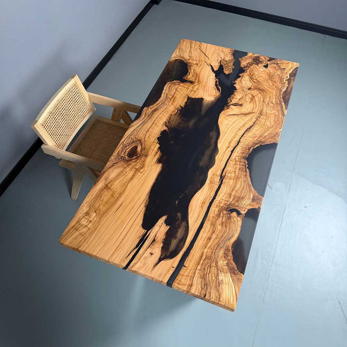 Wooden dining table with black resin inlay and a chair on a gray floor.