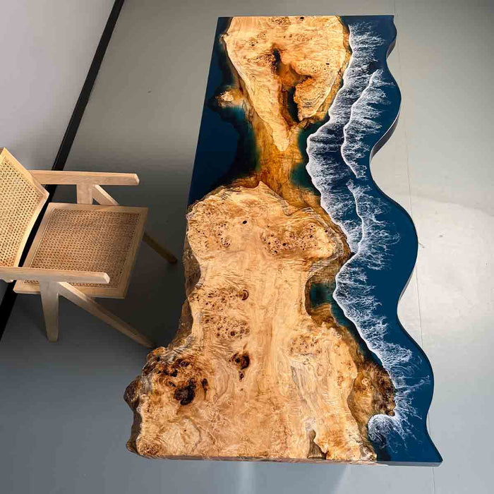 Wooden table with a natural finish and blue resin design, next to a wicker chair.