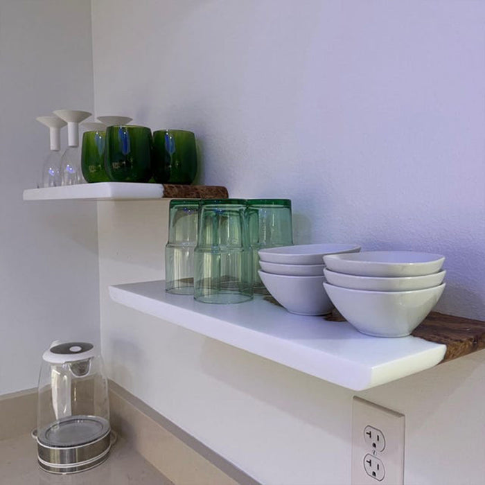 White shelves with green glasses and white bowls against a white wall.