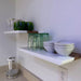White shelves with green glasses and white bowls against a white wall.