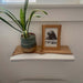 Small wooden shelf with a potted plant and framed picture against a white wall.