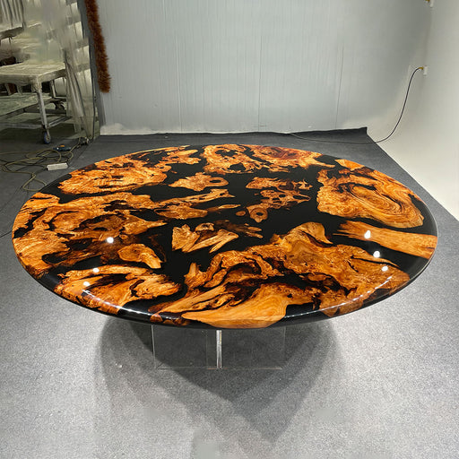 Round table with a unique wood and black resin design on a gray floor.