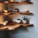 Wooden shelves with natural edges, candles, and small plants against a plain wall.