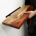 Handmade wooden shelf with a natural finish held by a person against a white wall.