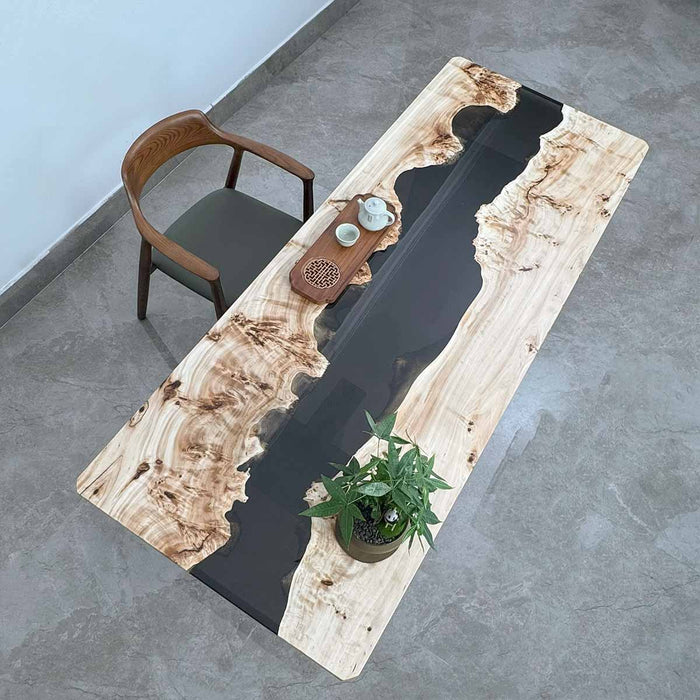 Wooden table with black resin inlay and a chair on a concrete floor.