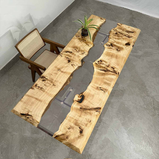 Wooden dining table with a natural, uneven surface in a room with a chair and plant.