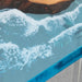 Close-up of a glass table with water and a rock, viewed from above.