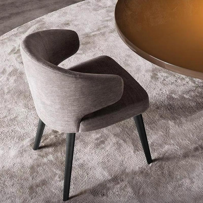 Gray upholstered chair on a textured rug with a round wooden table in the background