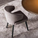 Gray upholstered chair on a textured rug with a round wooden table in the background