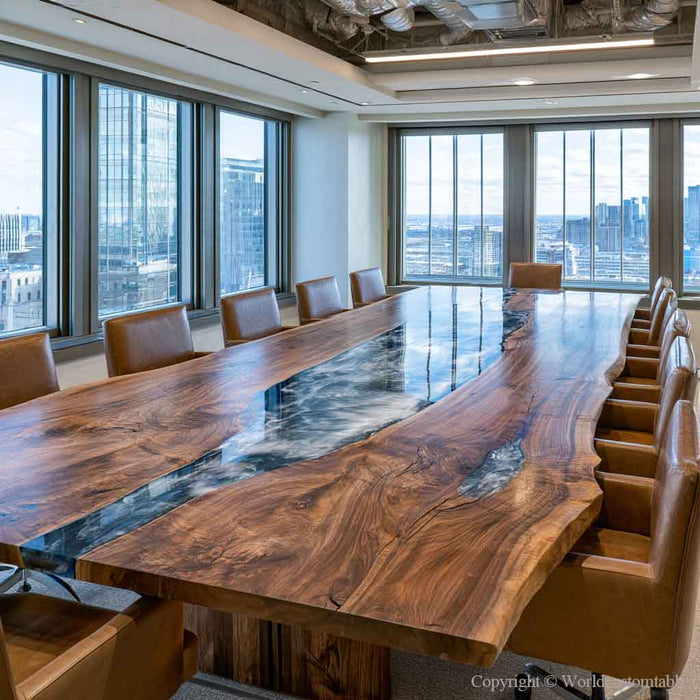 A large modern conference table with a live-edge natural wood top and a glossy dark resin river inlay, surrounded by brown leather chairs in a high-rise office with floor-to-ceiling windows.
