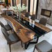 A modern live-edge wooden dining table with a glossy black center channel, surrounded by gray upholstered dining chairs in a contemporary dining room setting.