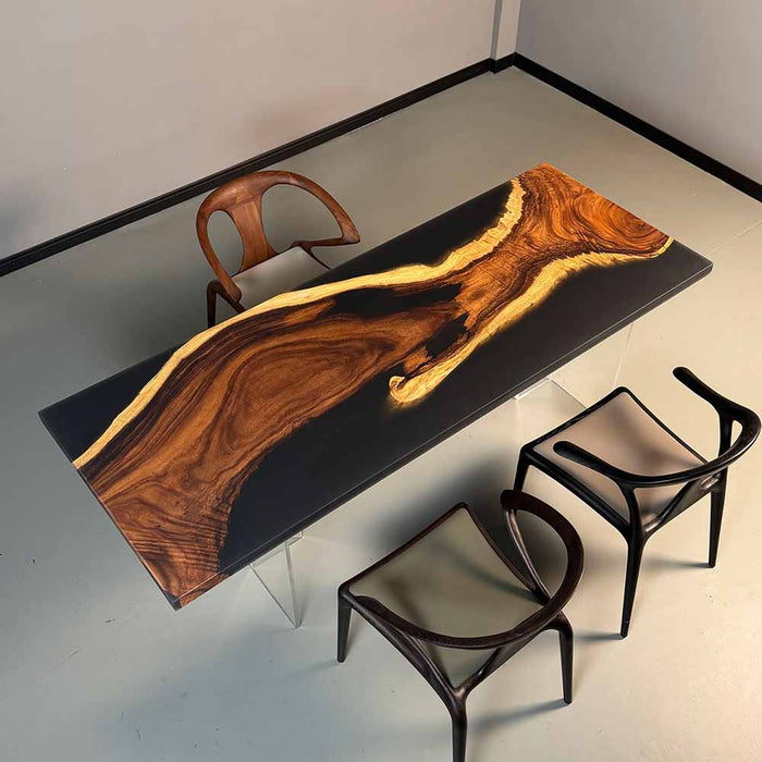 Wooden dining table with black surface and natural wood grain, accompanied by modern chairs.