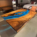 Solid walnut slab table with embedded blue glowing resin, viewed in a cozy setting.