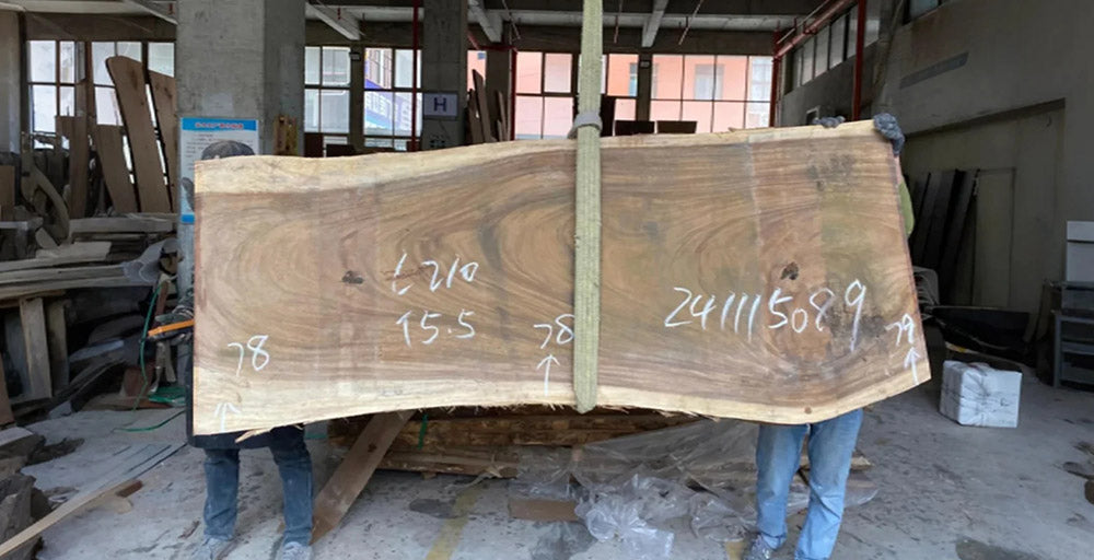 Large wooden slab with measurements held by two people in a workshop.
